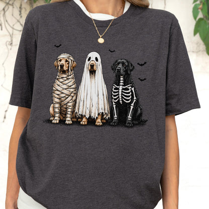 May include: A dark charcoal gray short-sleeve t-shirt featuring a graphic of three dogs dressed in Halloween costumes. One dog is wrapped like a mummy, one is wearing a white ghost sheet, and one has a skeleton print on its black fur.