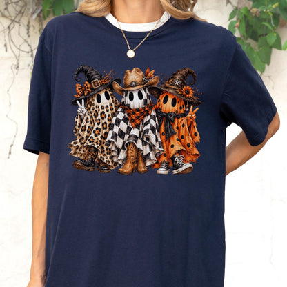 May include: A navy blue short-sleeve t-shirt featuring a graphic of three ghosts wearing hats. The left ghost has a leopard print sheet and boots, the center ghost has a checkered sheet and cowboy boots, and the right ghost has an orange polka dot sheet.