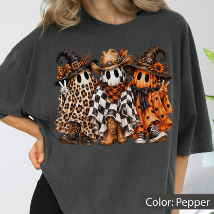 May include: A charcoal gray t-shirt featuring a graphic of three ghosts. The left ghost wears a leopard print sheet and witch hat, the center ghost wears a checkered sheet and cowboy hat, and the right ghost wears an orange polka dot sheet.