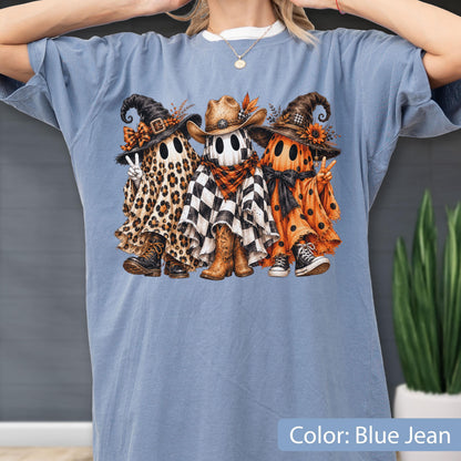 May include: A blue jean colored t-shirt featuring a graphic of three ghosts. The left ghost wears a leopard print sheet, witch hat, and boots. The center ghost wears a black and white checkered sheet, cowboy hat, and boots. The right ghost wears an orange polka dot sheet, witch hat, and sneakers.