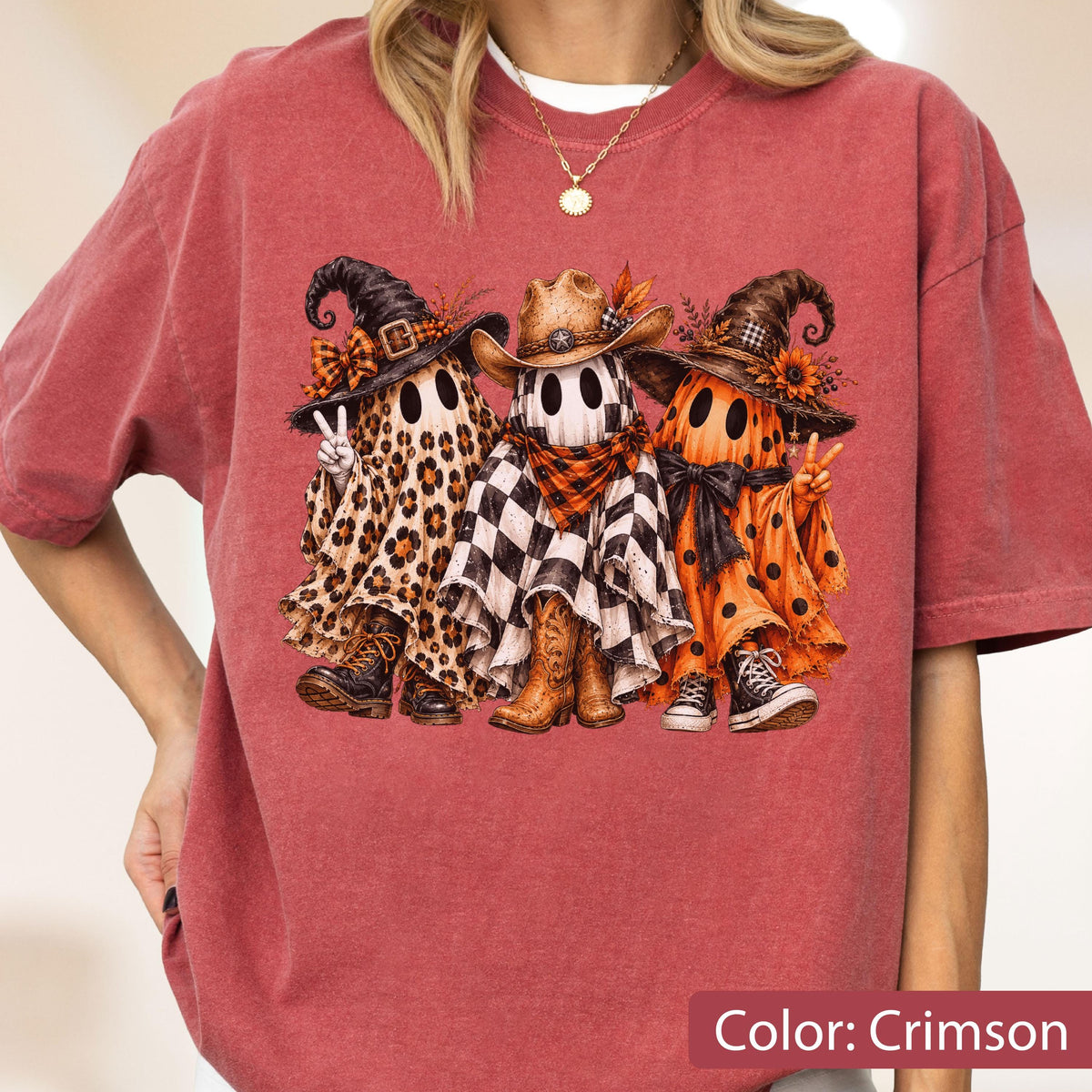 May include: A crimson t-shirt featuring a graphic of three ghosts wearing hats. The left ghost has a leopard print sheet and combat boots, the center ghost has a checkered sheet and cowboy boots, and the right ghost has an orange polka dot sheet.